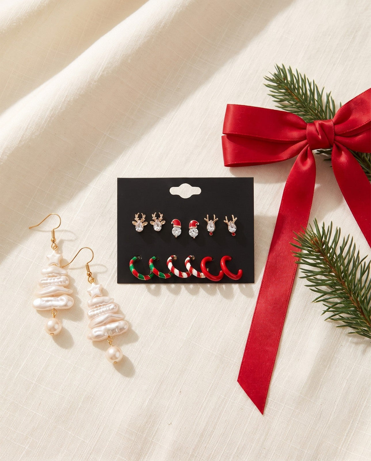 Christmas earrings and a red ribbon bow clip on ivory linen with a pine sprig