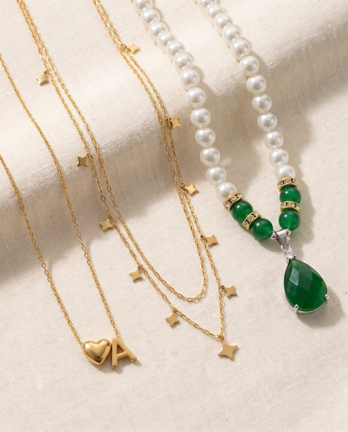 Free necklaces on ivory linen: an initial necklace, a layered star necklace and a faux pearl necklace