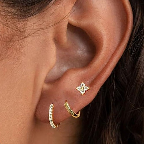 Gold tone earring set on an ear: a small hoop with clear stones, a plain hoop and a flower stud