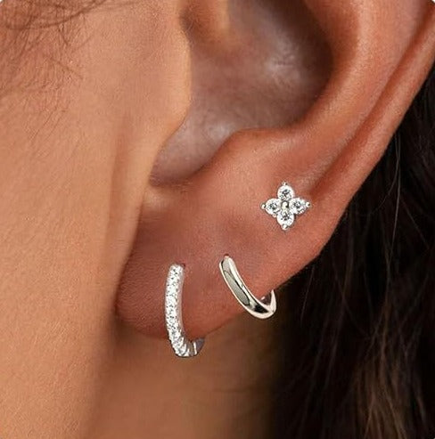 Silver tone earring set on an ear: a small hoop with clear stones, a plain hoop and a flower stud