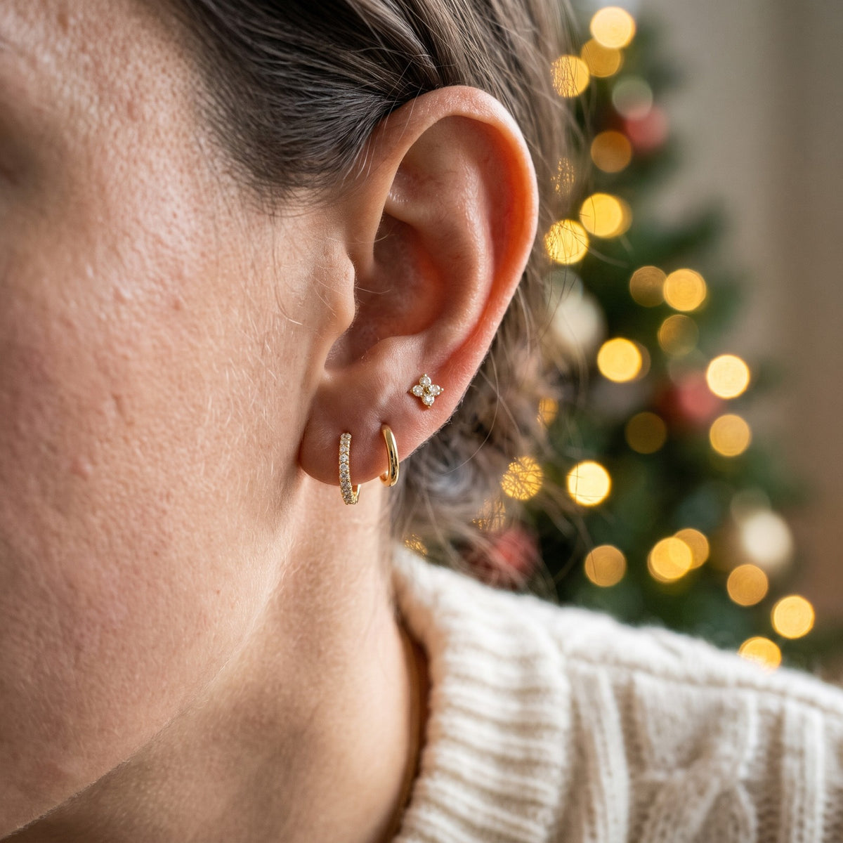 Gold tone earring set worn in one ear: a hoop with clear stones, a plain hoop and a flower stud
