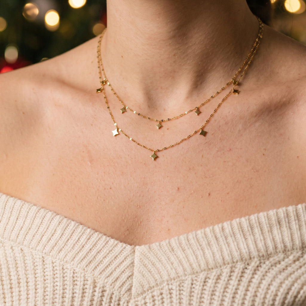 Layered gold tone necklace with star charms, worn with a cream sweater