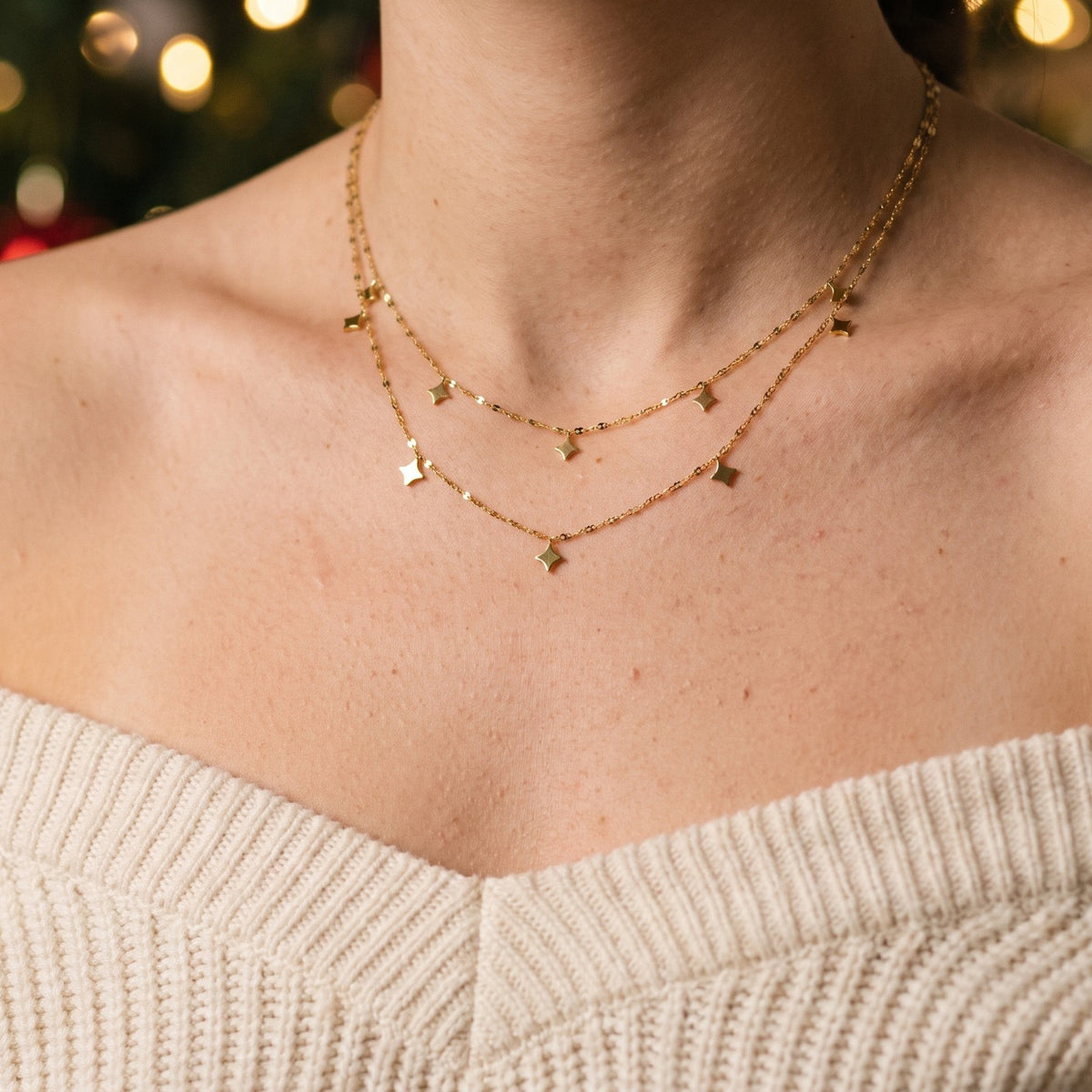 Layered gold tone necklace with star charms, worn with a cream sweater