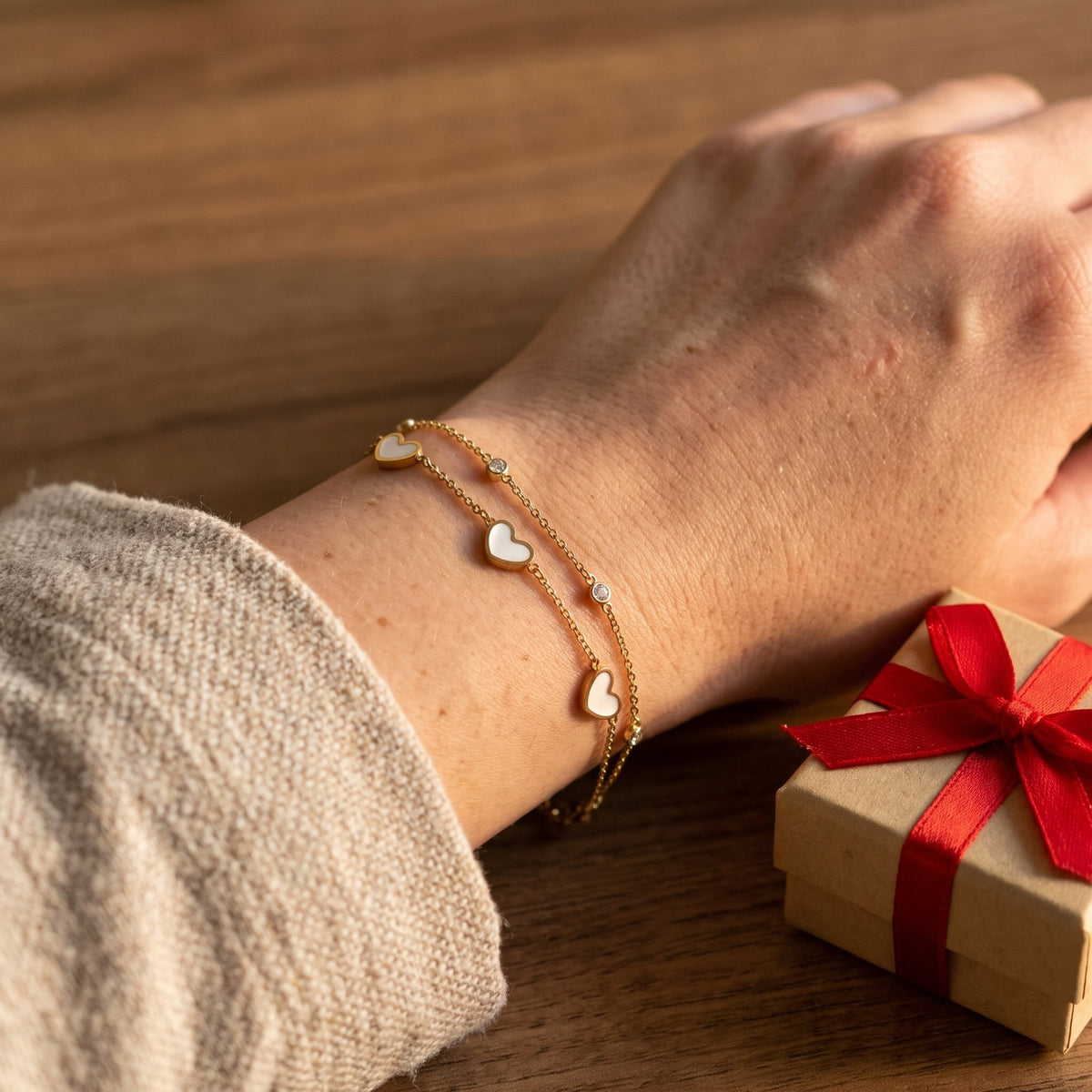 Gold tone two strand heart bracelet worn beside a wrapped gift