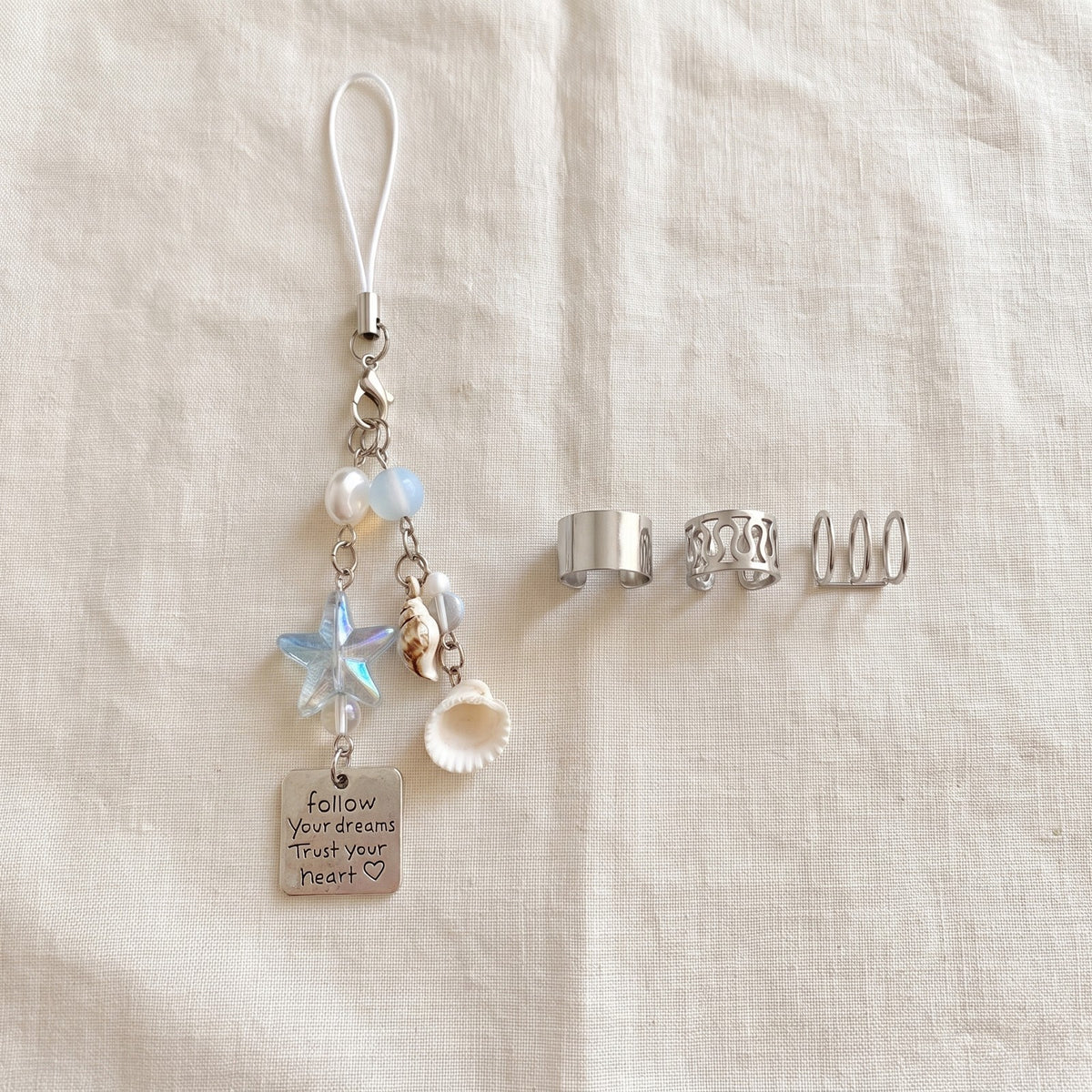 Beaded phone chain on ivory linen beside silver tone ear cuffs