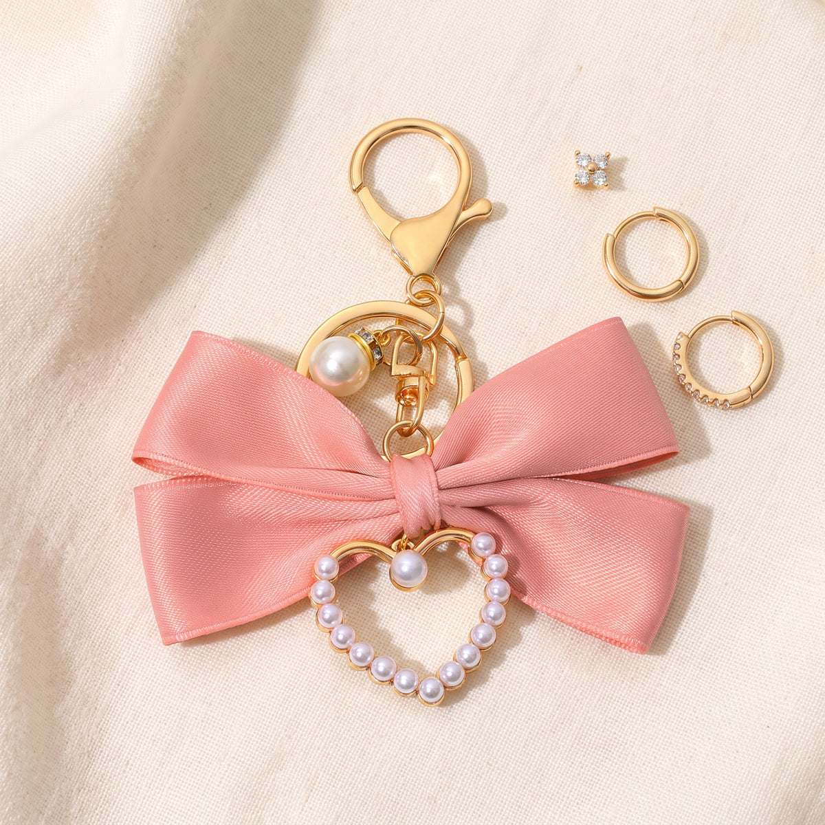 Pink bow charm on ivory linen beside the Huggie earrings