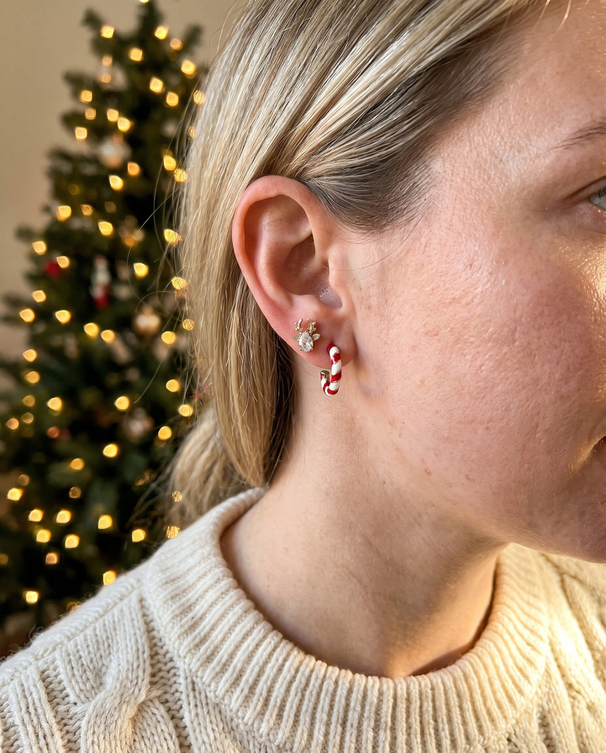 Worn together: a reindeer stud and a red and white striped hoop, a Christmas tree behind