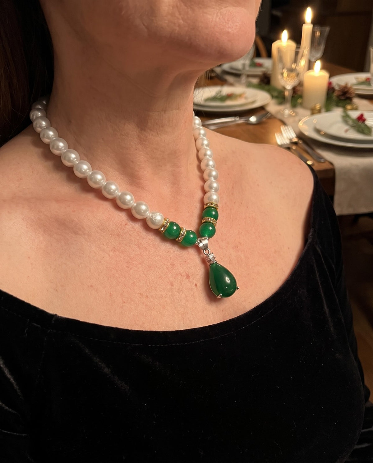 Faux pearl necklace with a green teardrop pendant worn with a black velvet top