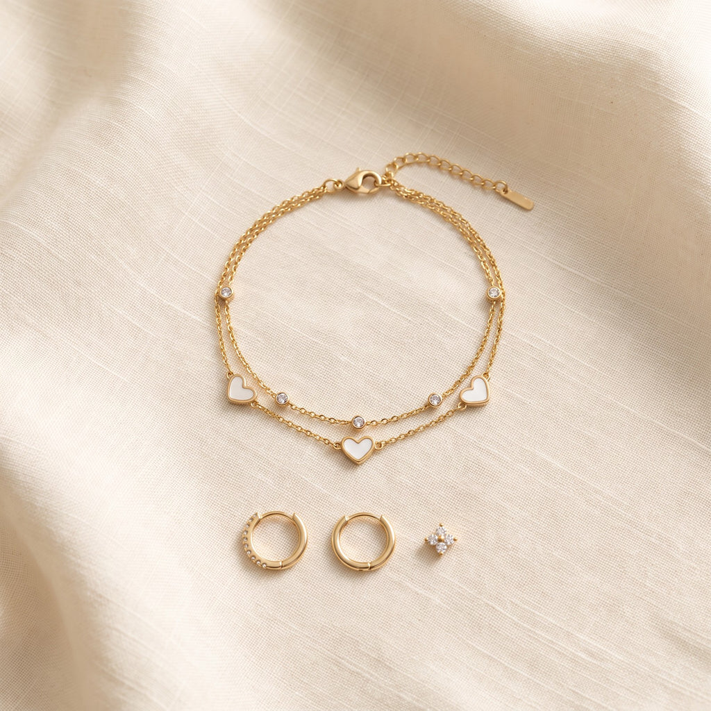 Gold tone heart bracelet on ivory linen beside the Huggie earrings