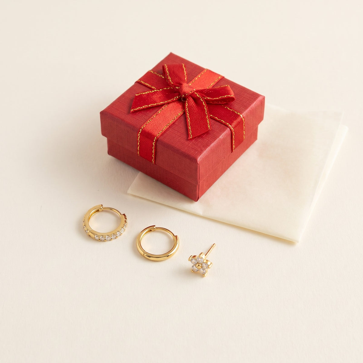 The three Huggie earrings beside a red gift box