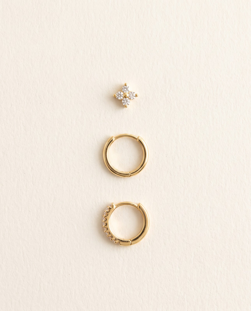 The three Huggie earrings laid out in wearing order: flower stud, plain hoop, hoop with clear stones