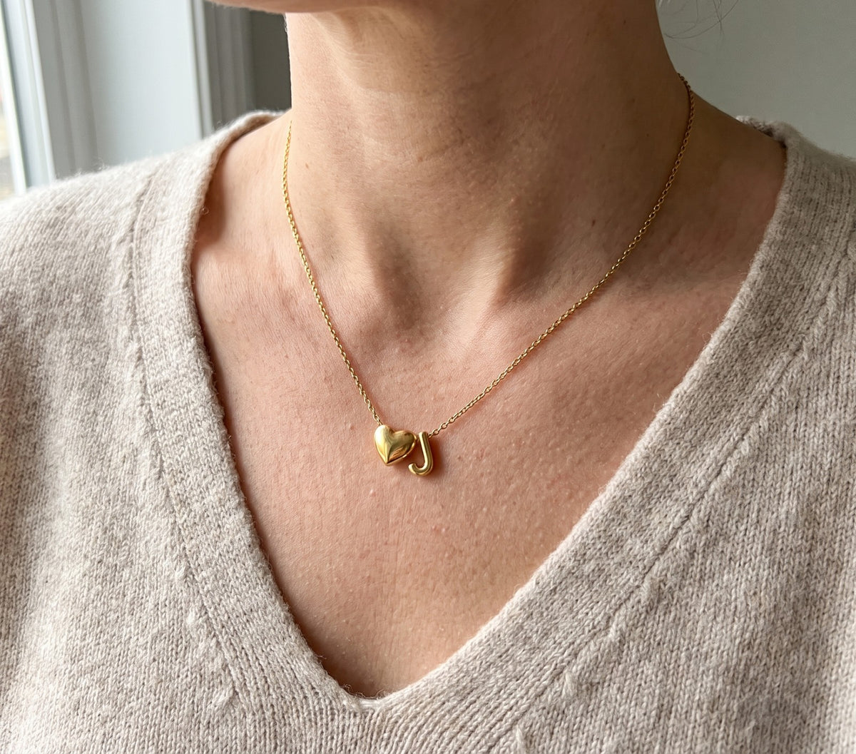 Initial necklace worn, a small heart beside the letter J