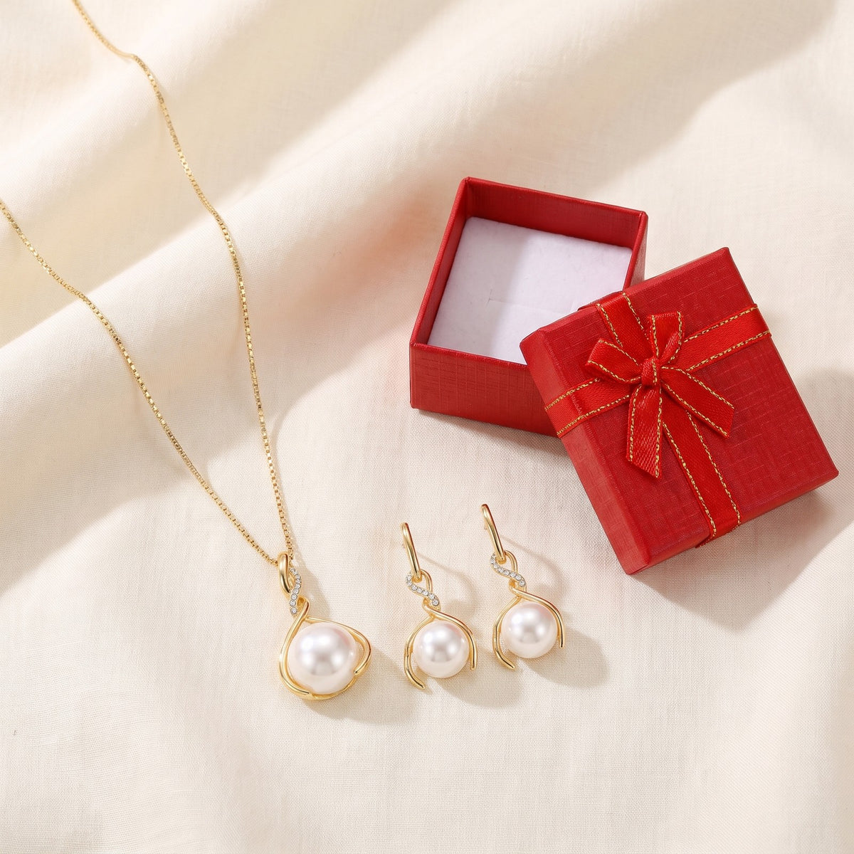 Faux pearl pendant and drop earrings on ivory linen beside a red gift box