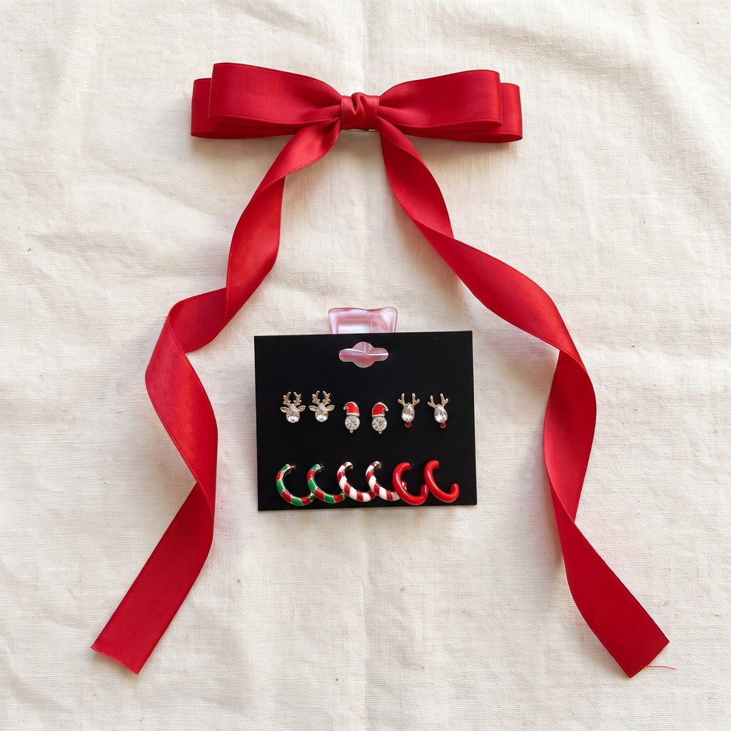 Red ribbon bow clip on ivory linen beside the Christmas earring card