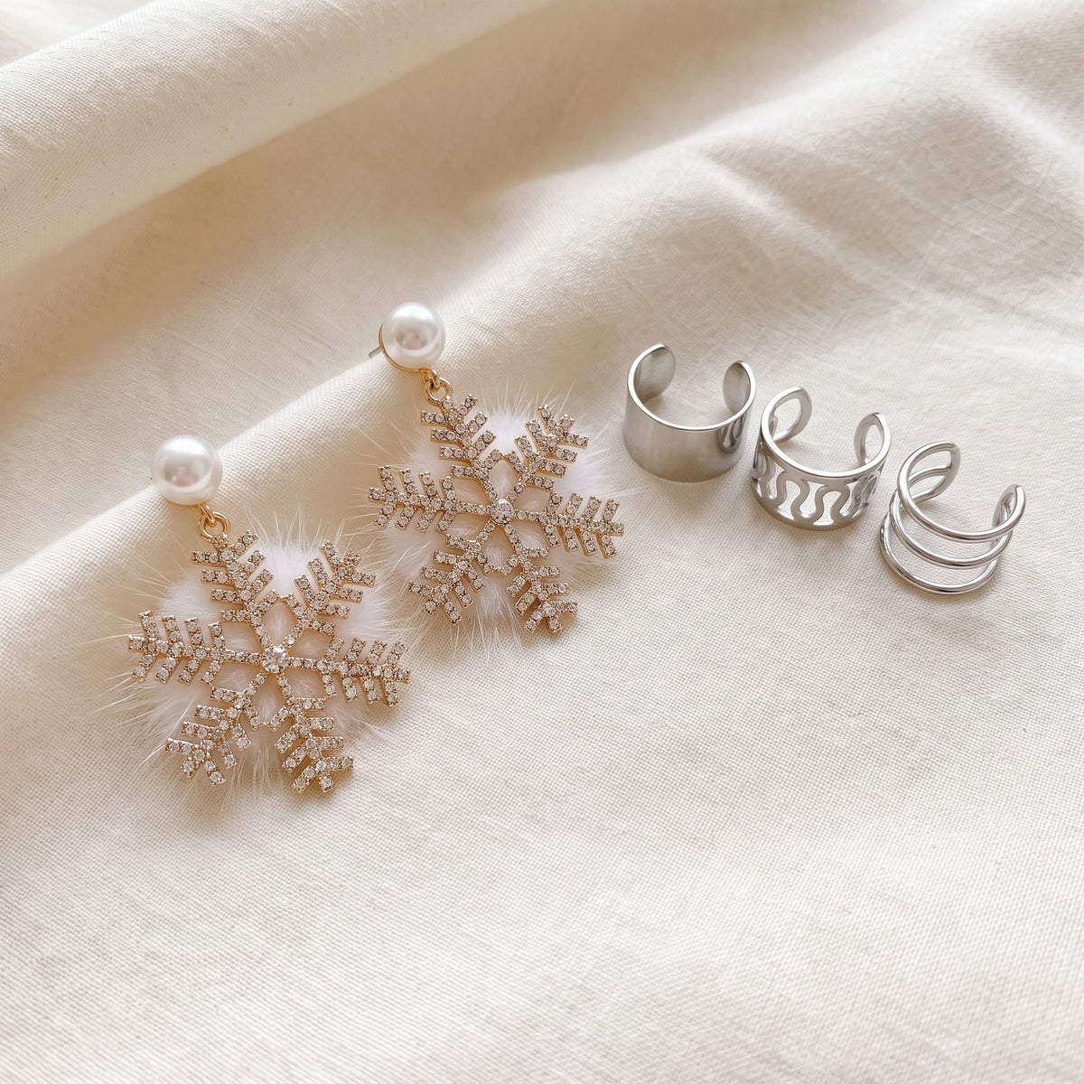 Snowflake earrings on ivory linen beside silver tone ear cuffs