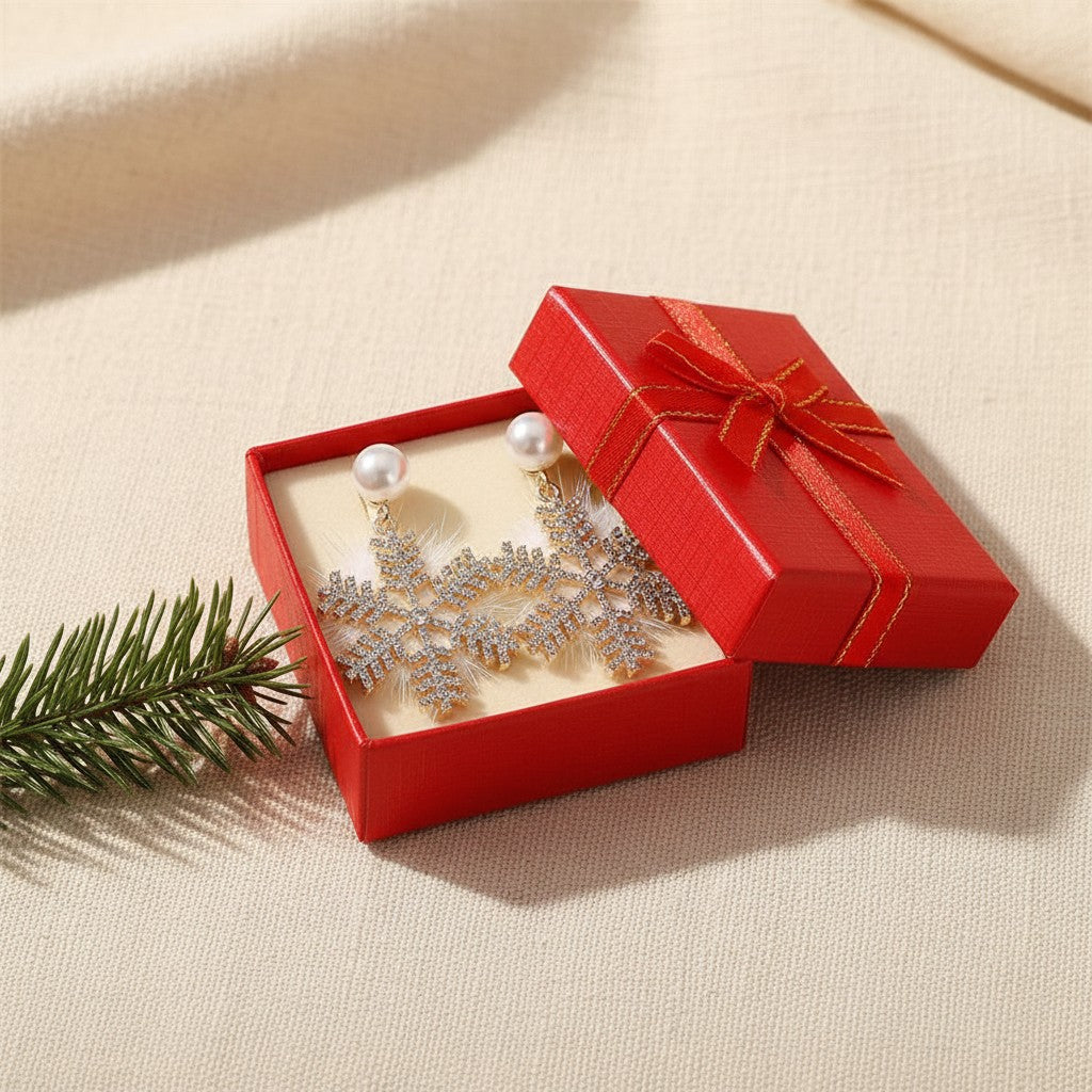 Snowflake earrings in an open red gift box beside a pine sprig