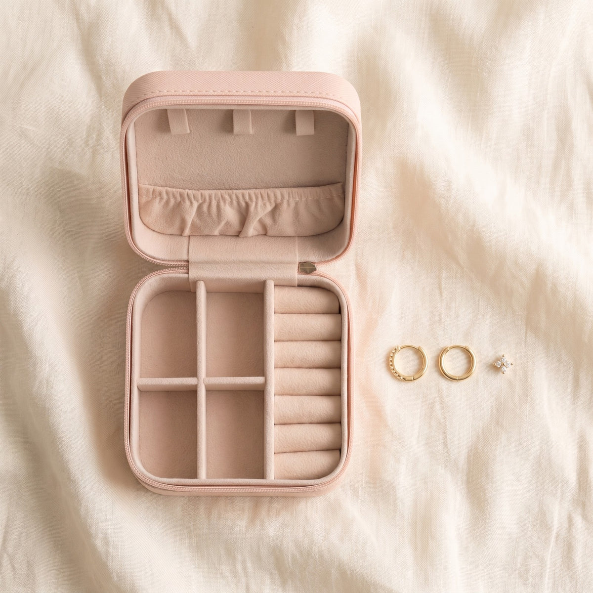The pink travel jewelry case open on ivory linen beside the Huggie earrings